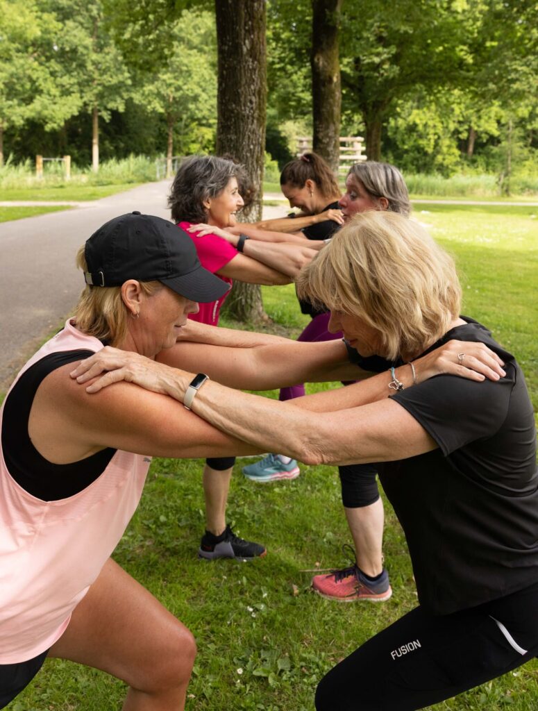 Vijf vrouwen doen een squat oefening samen in een groene parksetting.